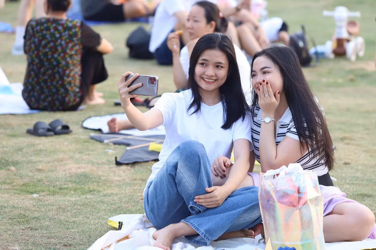 Đôi bạn tranh thủ check-in trong lúc ngồi trên bãi cỏ xem thả diều.