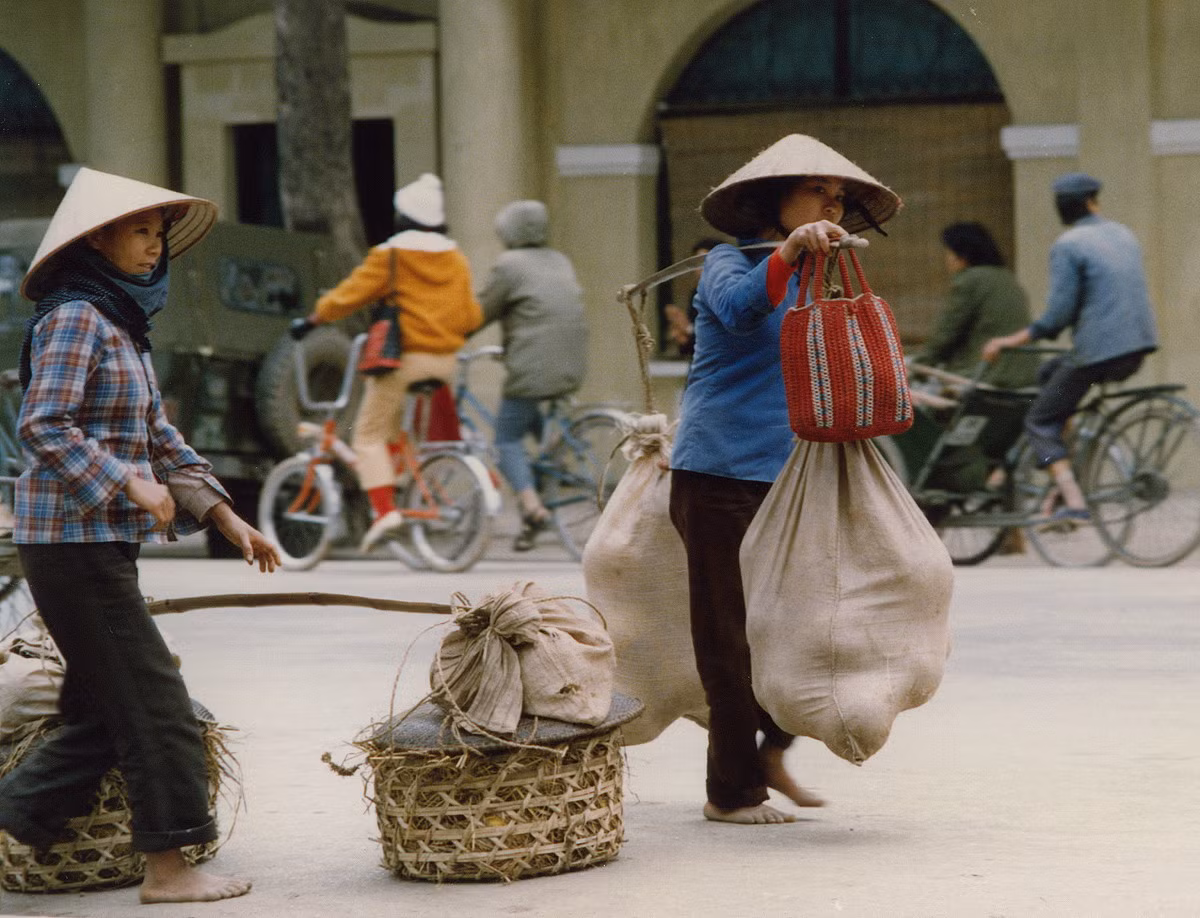 Hai phụ nữ gánh bưởi ngang qua tòa nhà "hàm cá mập", lúc này chưa xây xong, ở ngã 5 bờ hồ.