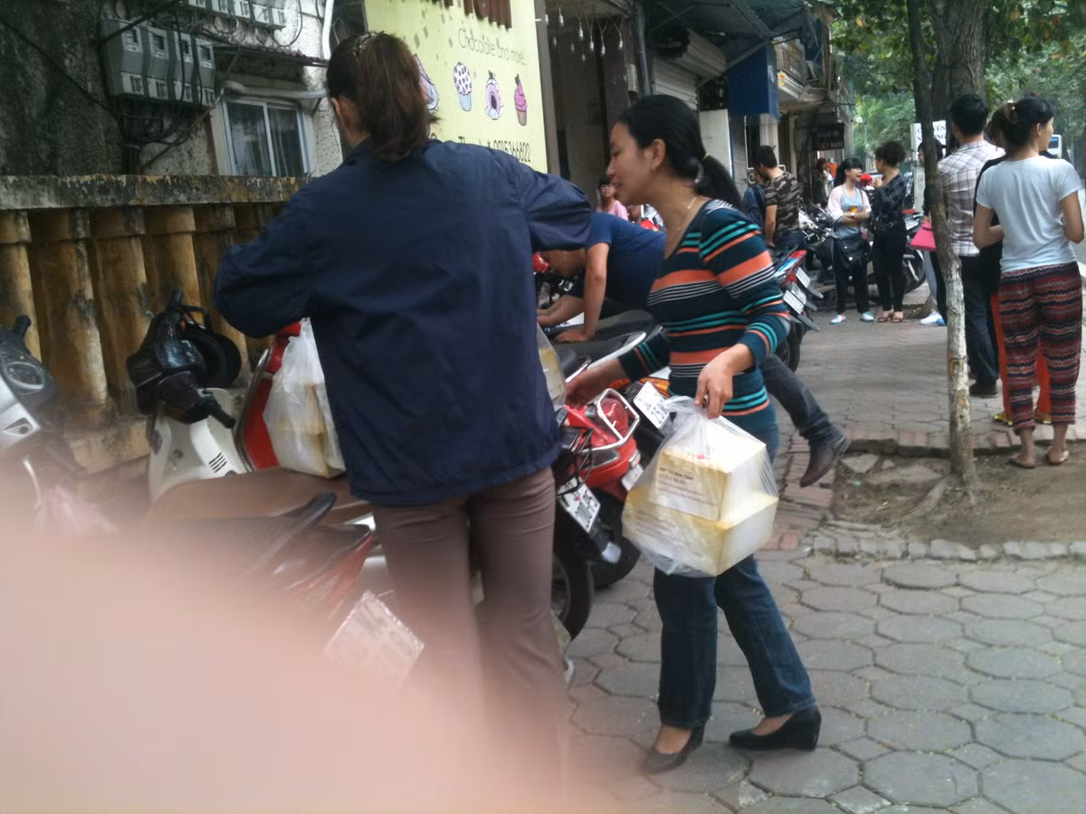 Khuôn mặt hớn hở của 2 vị khách khi mua được vài hộp bánh từ cửa hàng, trong khi dòng người đang xếp hàng chờ đợi đến lượt được phục vụ.