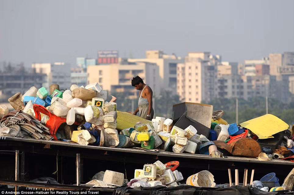 Một người đàn ông làm việc trên một mái nhà ở khu ổ chuột Dharavi với đầy chai nhựa và đồ phế liệu.