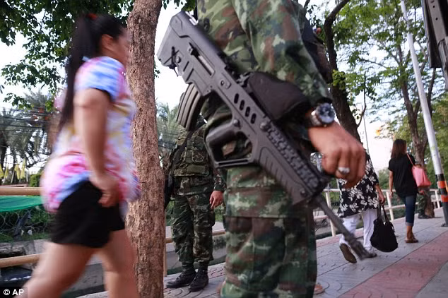 Người dân đi qua các binh sĩ trên đường phố ở Bangkok, sau khi quyết định thiết quân luật có hiệu lực.