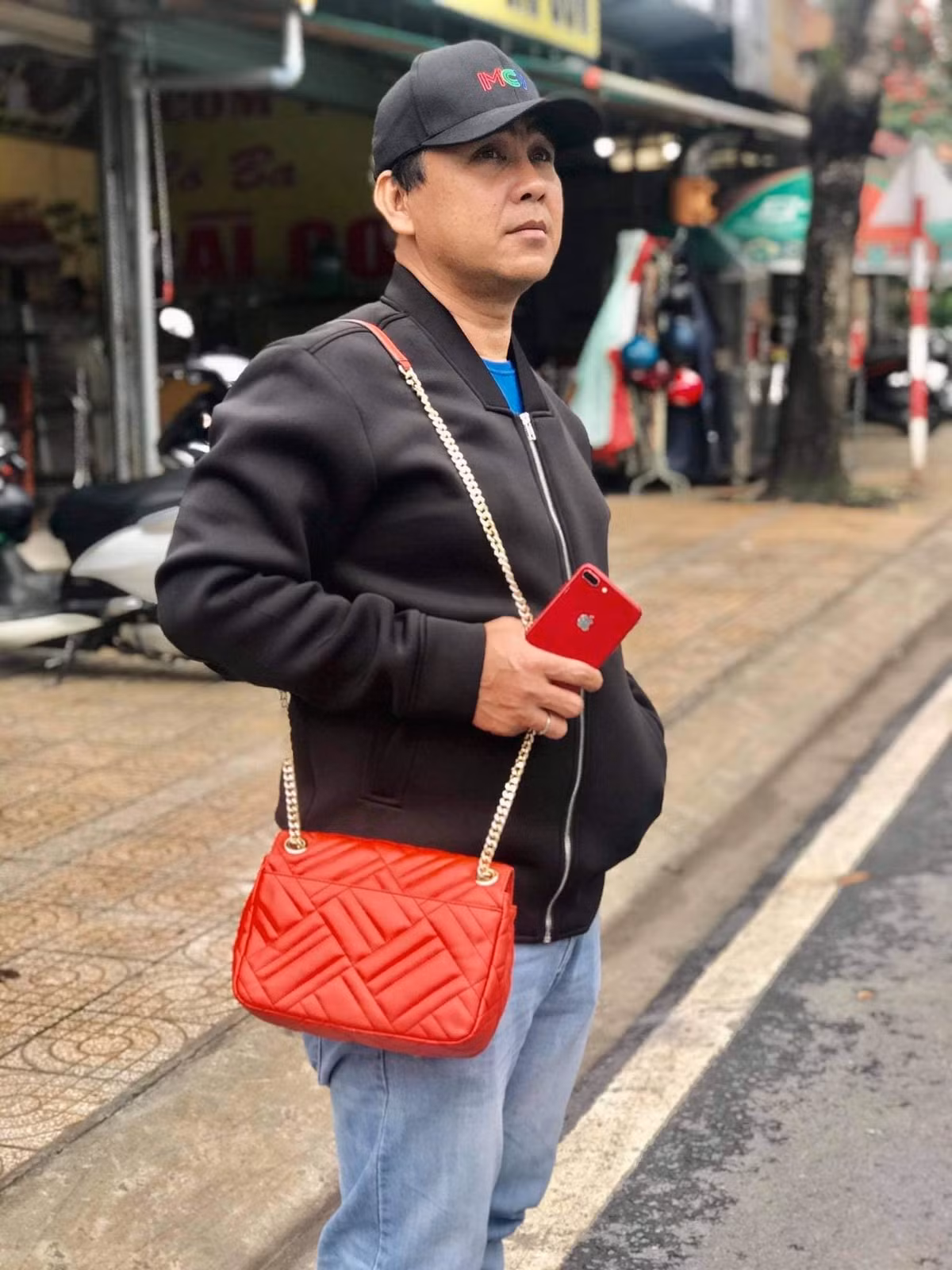 Quyền Linh tạo dáng chụp ảnh hài hước khi khoác túi xách cho vợ.