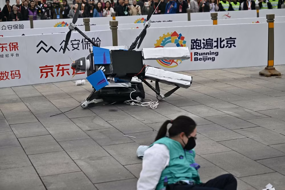 Con robot này và người nữ kỹ sư cùng ngã sóng soài trên đất. Các thành phần và bộ phận có thể dễ dàng bị hỏng khi chạy, vì vậy các nhà phát triển đã thay thế các bộ phận nhựa bằng kim loại và sử dụng vật liệu siêu bền nhưng đắt tiền.