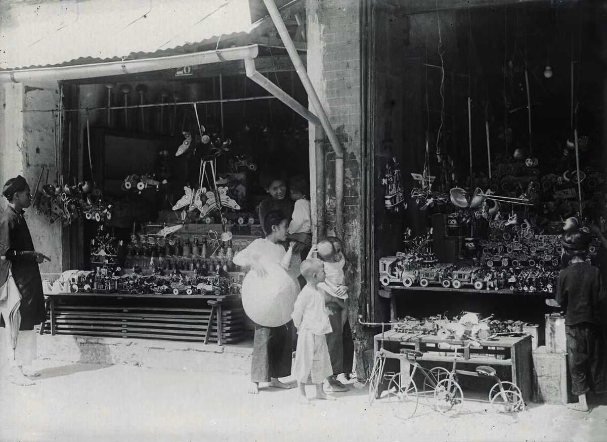 Trẻ em tại một cửa hàng đồ chơi ở Hà Nội thập niên 1920. Có hai chiếc xe đạp trẻ em đóng bằng sắt (phía dưới, bên phải), một món đồ chơi "xa xỉ" của trẻ em thời đó.