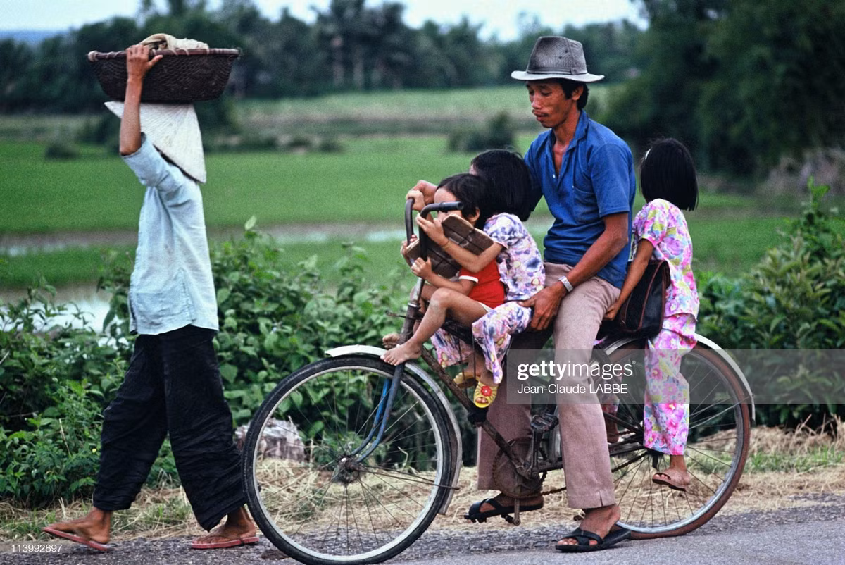 Người đàn ông chở ba đứa trẻ bằng xe đạp trên đường quê.