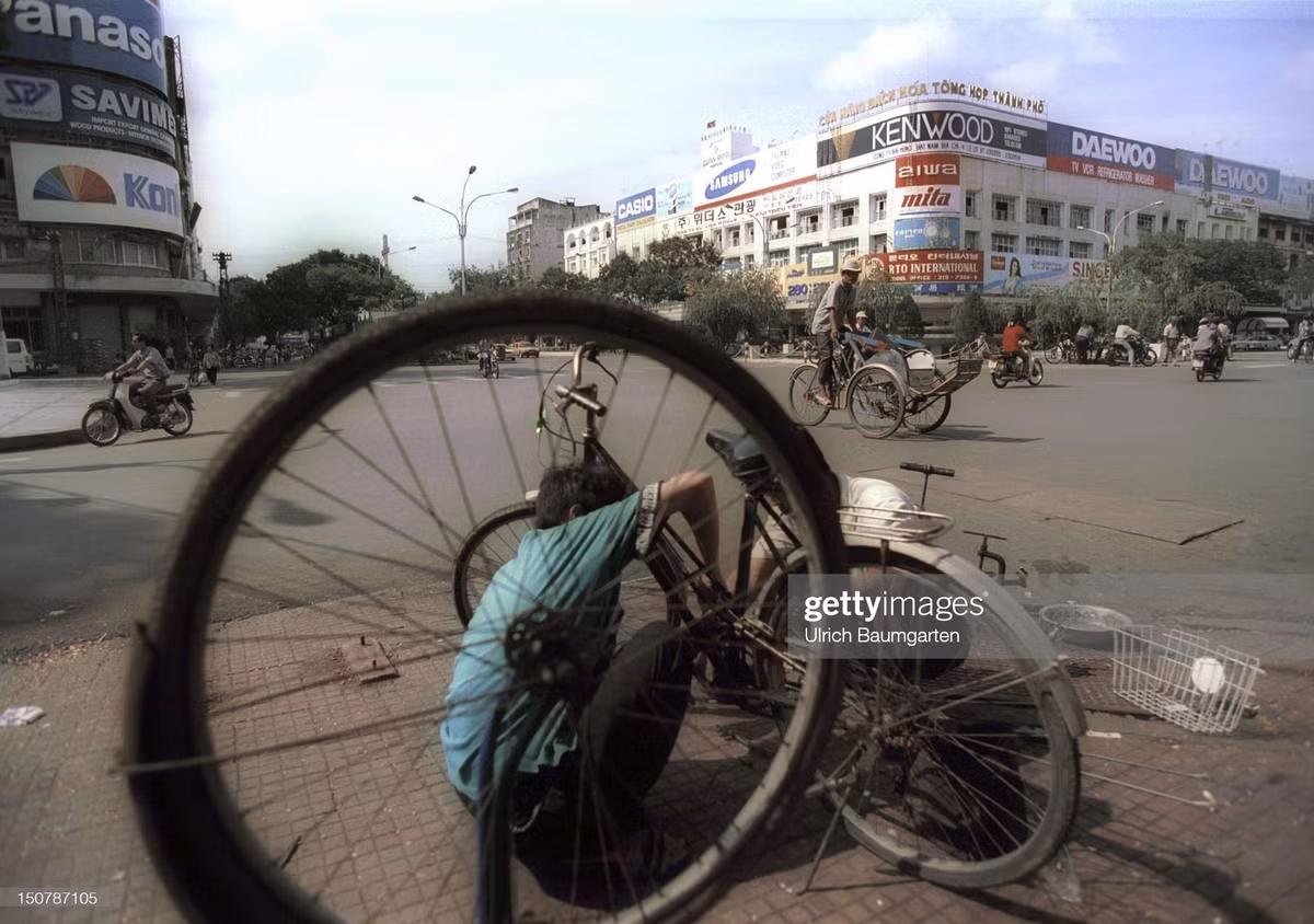 Người thợ sửa xe đạp hành nghề ở vỉa hè ngã tư Lê Lợi - Nguyễn Huệ, chéo góc với thương xá TAX - lúc này được gọi là Cửa hàng bách hóa tổng hợp thành phố.