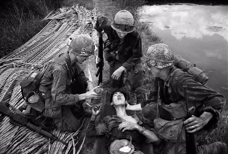 Lính Mỹ đưa nước uống cho một chiến sĩ Giải phóng, do khâm phục tinh thần quả cảm của đối phương. Anh đã chiến đấu trong ba ngày với một đoạn ruột bị sổ ra, được úp trong một chiếc bát buộc ở bụng trong chiến dịch Mậu Thân 1968. Ảnh: Philip Jones Griffiths/Magnum.