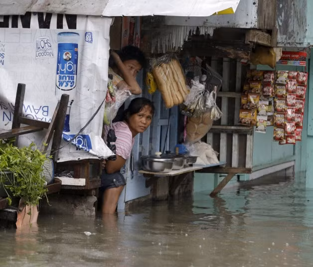 Chủ một cửa hàng tạp hóa nhìn ra đường phố ngập lụt ở ngoại ô Quezon, Philippines.