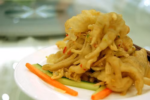 Cho chân gà vào tô, nêm mắm, chanh, hành, ớt, tỏi, đường, dùng tay bóp nhẹ cho gia vị thấm vào thịt. Cuối cùng bạn trộn chân gà với là húng, hành lá, ngò và gạo rang.