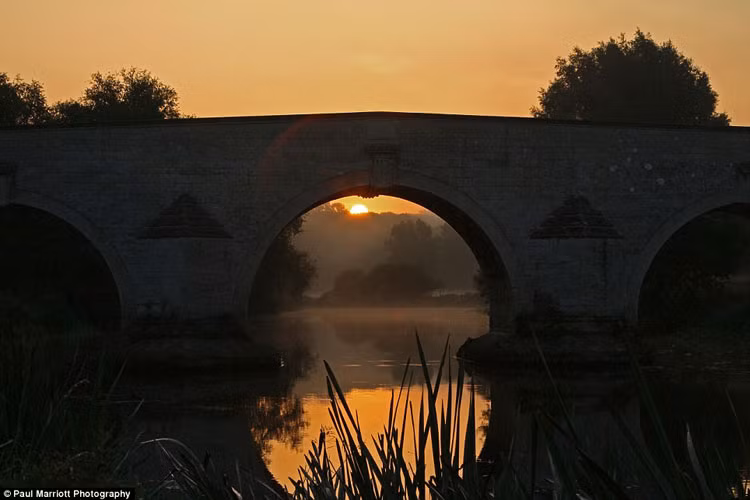 Mặt trời mọc trên cầu Milton Ferry trên sông Nene gần Peterborough, Cambridgeshire.