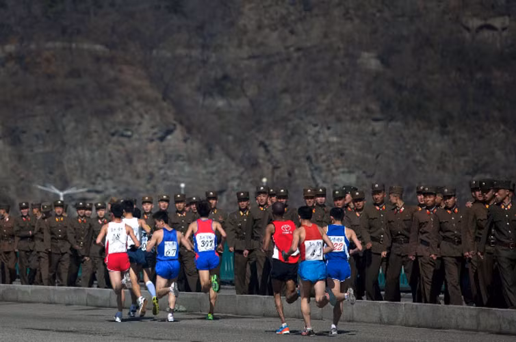 Các vận động viên Marathon chạy qua một nhóm binh sĩ khi băng qua cây cầu. Triều Tiên tổ chức giải Marathon Mangyongdae để kỷ niệm sinh nhật nhà lãnh đạo Kim Nhật Thành.
