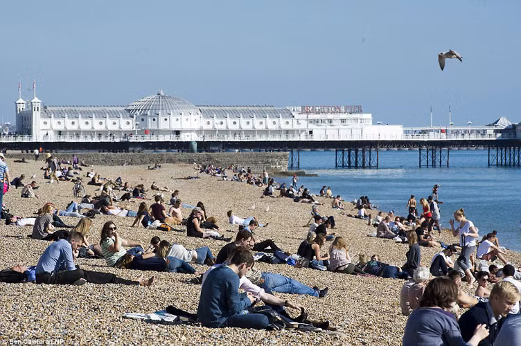 Các cặp đôi ngồi phơi nắng bên bãi biển Brighton, East Sussex trong nhiệt độ 20 độ C.
