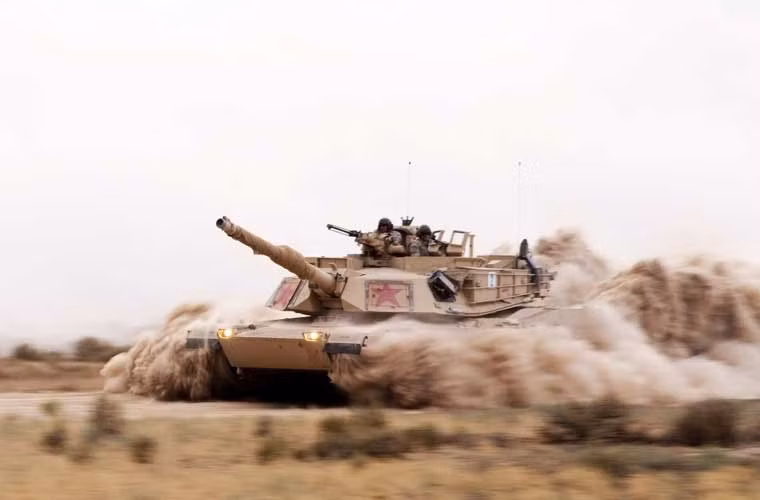 Chiếc xe tăng M1A1 và kíp lái thuộc Trung đoàn kị binh số 1 (Quân đội Mỹ) hành tiến làm cát bụi cuốn theo mù mịt.