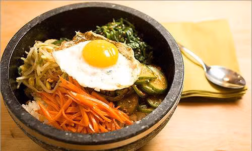 Cơm trộn Bibimbap. Để làm món cơm trộn này, trước hết phải phải làm chín thịt bò (hoặc thịt lợn), cà rốt, giá đỗ, rau cải, trứng ốp la. Cho cơm vào chảo hoặc bát, xếp xen kẽ các nguyên liệu đã làm chín vào, quả trứng sẽ xếp lên trên cùng. Rắc đều vừng và dầu vừng lên là được