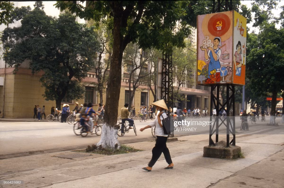 Trên vỉa hè bờ hồ Hoàn Kiếm, đối diện Bưu điện Hà Nội. Trên cột điện có tranh cổ động về Đại hội Đảng toàn quốc lần thứ VI, kỳ Đại hội đưa ra đường lối Đổi Mới cho đất nước.