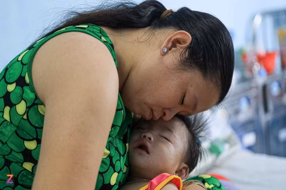 Bé Mỹ Duyên đi vào giấc ngủ trong vòng tay mẹ. Khóe miệng và cổ em vẫn còn đọng lại những vệt sữa vừa nôn ra. Những lần truyền dịch liên tục, cơn đau từ các vết loét bên trong miệng dường như quá sức với đứa trẻ 10 tháng tuổi. Ba hôm trước, bé Duyên sốt cao, nằm bệnh viện tuyến tỉnh không thuyên giảm. Chị Trần Mỹ Xuyên (40 tuổi) sốt ruột, gác lại công việc, quyết cho con lên Bệnh viện Nhi đồng 1 để chữa trị. “Bình thường con rất hay cười nhưng giờ đau quá chỉ biết khóc thôi. Mong sao con sớm khỏe”, chị Xuyên nói.