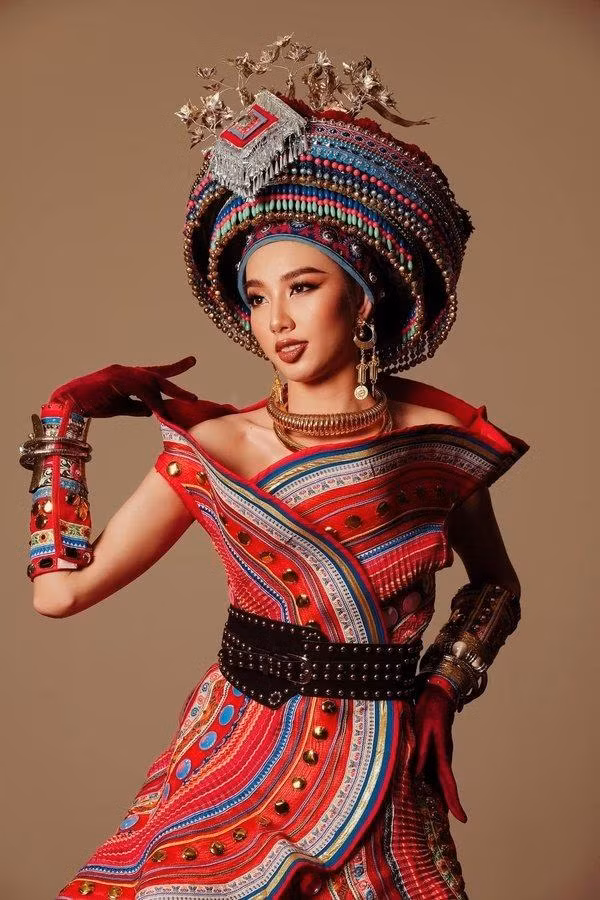 Thùy Tiên đầy bí ẩn và quyến rũ khi diện trang phục dân tộc của tỉnh Chiang Mai. Trang phục được làm chủ yếu bằng chất liệu thổ cẩm đầy họa tiết sặc sỡ, tạo điểm nhấn với phần nhún bèo và chiếc đai lưng đen bản to, kết hợp cùng chiếc mấn cực quyền lực và hoành tráng.