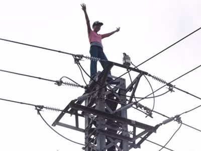 Trong khi đó, trên đỉnh cột điện, người phụ nữ vẫn giơ tay múa, múa mệt lại ngồi nghỉ.