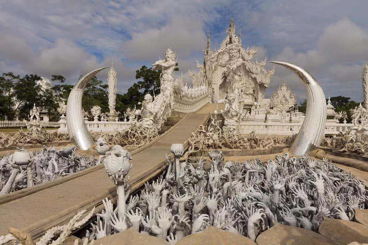 Về tổng thể, Wat Rong Khun giống như một công trình hiện ra từ thế giới cổ tích. Để đi đến gian chính điện của ngôi chùa, du khách sẽ phải đi qua một cây cầu đặc biệt, phía bên dưới là hàng trăm bàn tay đang vươn lên cao. Ảnh: Wikipedia.
