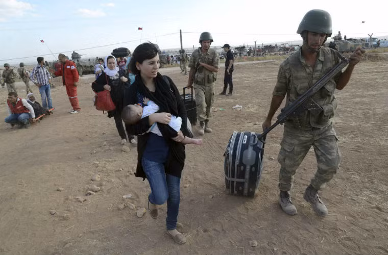 Binh sĩ Thổ Nhĩ Kỳ giúp phụ nữ Syria mang đồ đạc ở biên giới ngày 20/9. Binh sĩ Thổ Nhĩ Kỳ giúp phụ nữ Syria mang đồ đạc ở biên giới ngày 20/9.