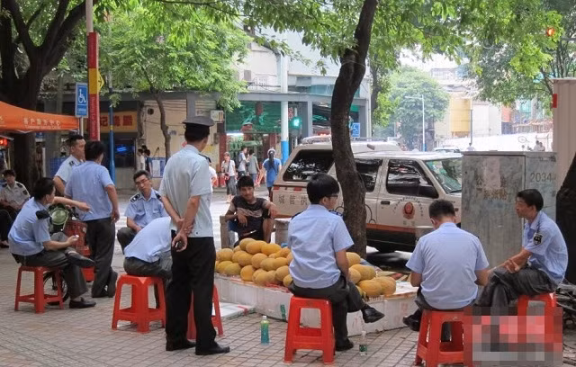 Một nhóm nhân viên an ninh, công an trật tự ngồi trước một quầy bán hoa quả trên vỉa hè nhưng không ai có hành động lỗ mãng.