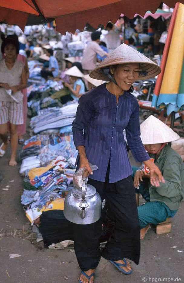 Người phụ nữ cầm ấm nước đi qua một hàng quần áo trẻ em.