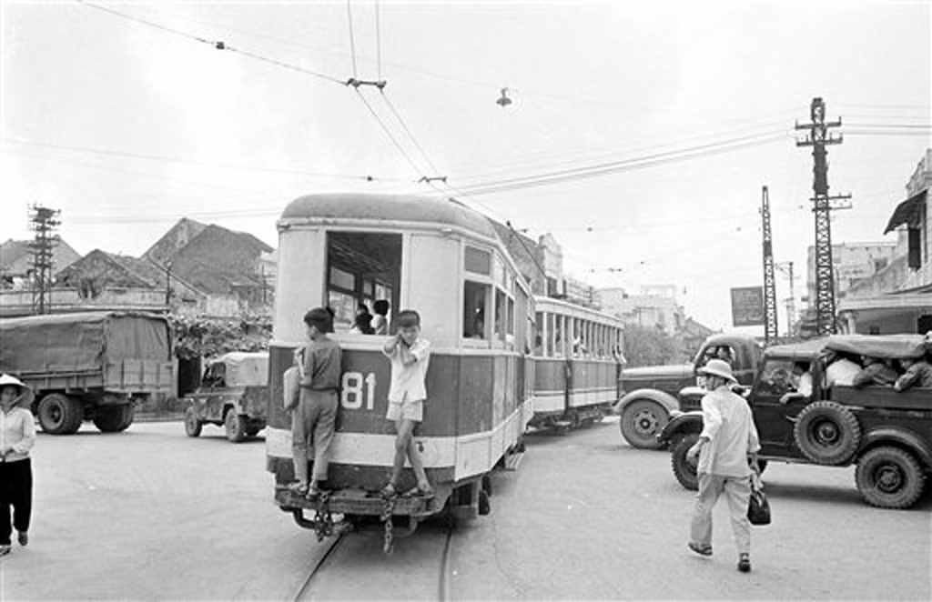 Hai thiếu niên đeo bám sau toa tàu điện bằng gỗ ở trung tâm Hà Nội, 4/4/1973. Không ai bận tậm đến việc xử lý các đối tượng "lậu vé" này.