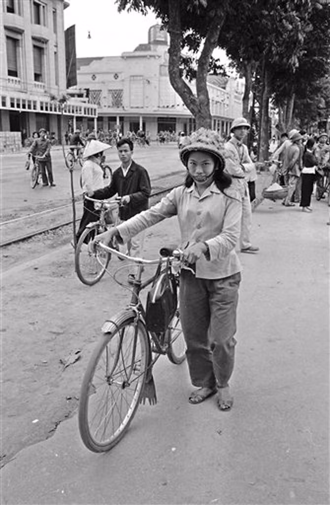 Một phụ nữ dắt xe đạp cạnh đường xe điện bên bờ hồ, phía xa là ngã tư Đinh Tiên Hoàng - Tràng Tiền, 21/3/1973.