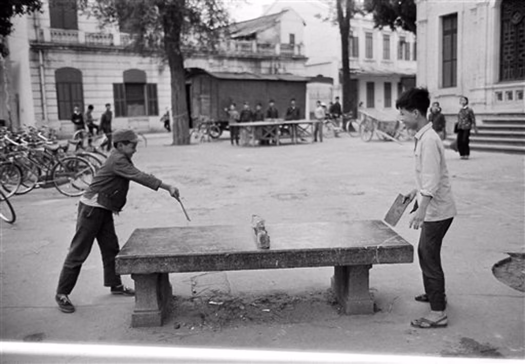 Hai chú bé chơi bóng bàn trên chiếc ghế đá cổ đối diện bờ hồ, góc Hàng Trống - Đinh Tiên Hoàng, những chiếc xe đạp được dựng gần đó, 27/3/1973.