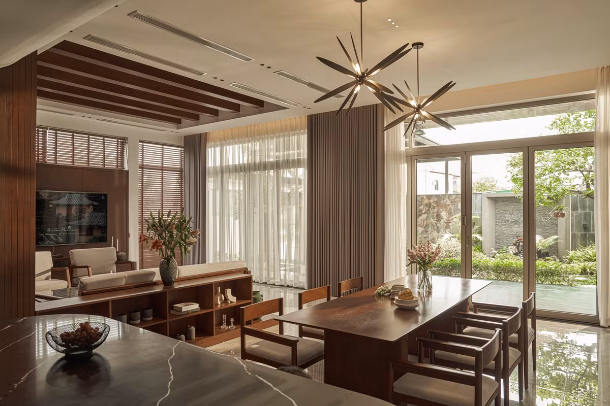 Khu vực tiếp khách ngăn với khu bếp bằng một kệ tủ nhỏ tiện dụng. Trần nhà được ốp gỗ, điểm xuyết hệ thống đèn trang trí tinh tế.