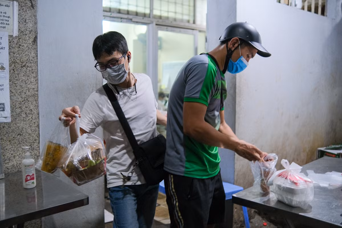 Anh Trương Bá Thành (phải), shipper quen của quán, nói thời gian này, anh có thể chạy tới 30 đơn/tối, gấp đôi ngày thường. Đổi lại, anh cũng phải bỏ đam mê xem bóng đá sang một bên. "Lấy đâu thời gian xem. Lúc tôi đi làm về cũng đã 3-4h rồi, chỉ có ngủ lấy sức để đêm đi tiếp", anh tâm sự.
