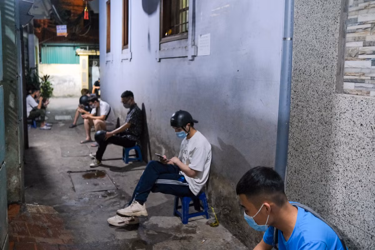 Các shipper ngồi hàng dài khi đồng hồ đã điểm gần 0h. Thời điểm này là lúc nhộn nhịp nhất do các trận đấu Euro 2020 diễn ra vào khung 23h và 2h. Trong thời điểm dịch bệnh còn diễn biến phức tạp, các shipper được yêu cầu giữ khoảng cách và đeo khẩu trang khi chờ đơn.