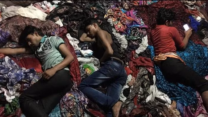 Một đứa trẻ làm việc trong nhà máy may mặc ở Dhaka, Bangladesh. Để tiết kiệm chi phí, nhiều nơi sử dụng lao động trẻ em một cách bất hợp pháp.