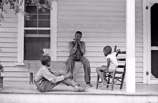 Các cậu bé da màu ngồi chơi bên hiên nhà khi không phải làm việc trên đồng. Ảnh: Arthur Rothstein.