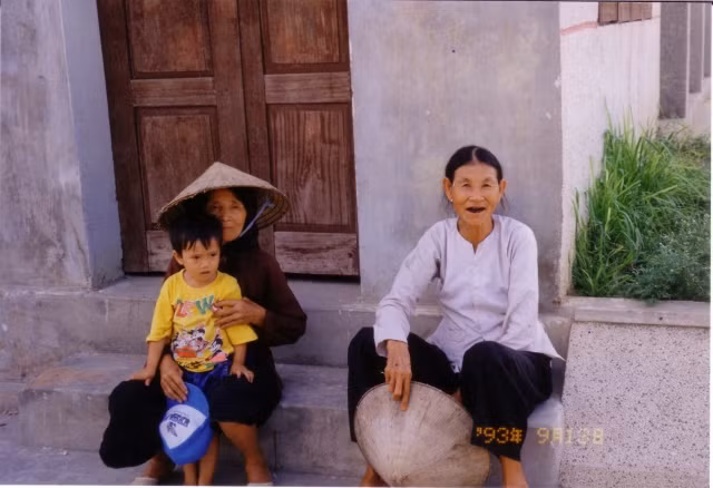 Hai cụ bà và em bé trước hiên nhà.