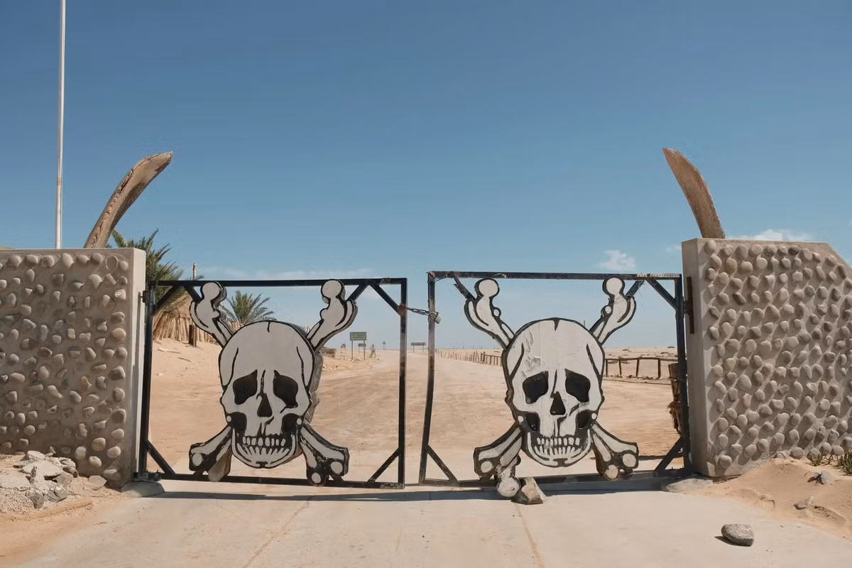 Cổng Ugab, lối vào phía nam của bờ biển Skeleton, với hình ảnh cảnh báo về những nguy hiểm và điều kiện khắc nghiệt đang chờ đợi du khách ở phía bên kia. Điều kiện khắc nghiệt và khô hạn là lý do cho sự ra đời của tên gọi Skeleton (tạm dịch: bộ xương). Tới Skeleton, người ta sẽ nhìn thấy sự nổi bật của các bộ xương động vật và xác tàu đắm rải rác trên bờ biển. Nhiều loài động vật đã thử và thất bại, thậm chí là bỏ mạng khi cố gắng biến nơi này thành nhà hoặc điểm dạo chơi. Vùng đất này trở thành một trong những điểm du lịch khắc nghiệt, cô độc nhất hành tinh.