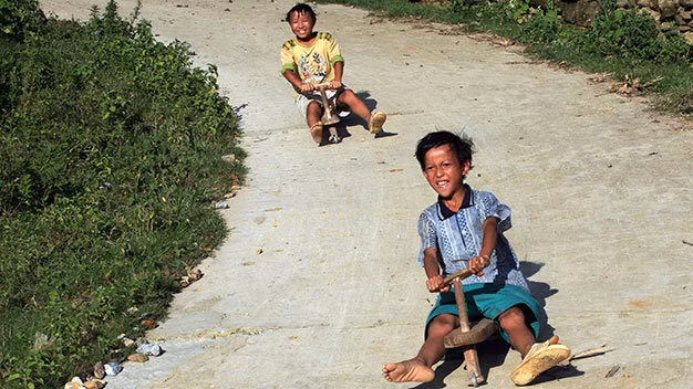 Hai em Sùng A Chung và Chàng A Ký 13 tuổi, dân tộc Mông, ở bản Hòa Sú Pản 1, xã Xứ Pán, Sa Pa (Lào Cai) thả dốc “chiếc xe máy” bằng gỗ - Ảnh: Lê Bích .