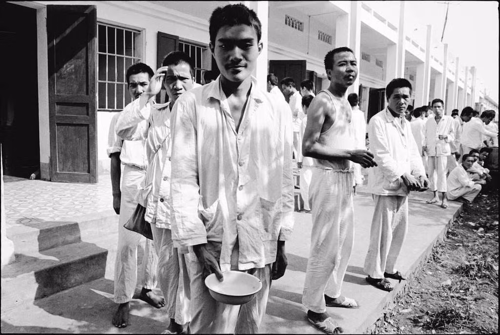 Bệnh nhân tâm thần xếp hàng nhận bữa ăn trưa ở "trại Trâu Quỳ". So với thời điểm những bức ảnh này được chụp, cơ sở vật chất của bệnh viện hiện tại đã có những bước tiến vượt bậc. Ảnh: Larry Towell/ Magnums.