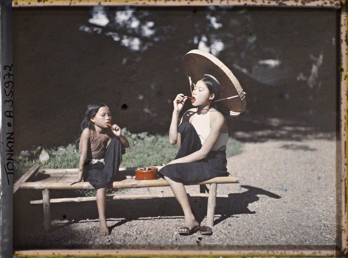 Bé gái và thiếu nữ ngồi trên chõng tre ăn trầu, nông thôn Bắc Bộ năm 1921.