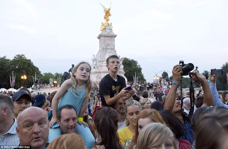 Một cậu bé và một cô bé được cha cõng trên vai, nhìn vào sân trước của cung điện Buckingham để tận mắt thấy thông báo Công nương Kate đã sinh hạ Hoàng tử.
