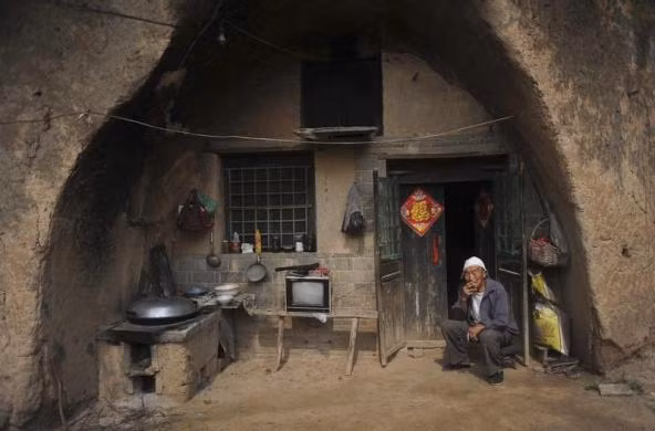 Một người đàn ông ngồi hút trước trước cửa ngôi nhà trong hang động của mình ở Yuncheng, tỉnh Sơn Tây, Trung Quốc.