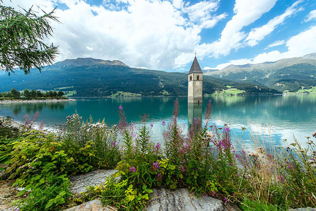 Hồ Reschen, Bolzano - Ý: Reschensee hoặc hồ Reschen là một hồ nhân tạo ở phần phía tây của Nam Tyrol, Ý, khoảng 2 km về phía nam của đèo Reschen, tạo thành biên giới với Áo, và 3 km về phía đông của sườn núi tạo thành biên giới với Thụy Sĩ. Hồ nổi tiếng với gác chuông của một nhà thờ thế kỷ 14 bị ngập nước, khi mặt nước đóng băng có thể đi bộ trên đó. Một truyền thuyết nói rằng trong mùa đông người ta vẫn có thể nghe thấy tiếng chuông của nhà thờ. Nhưng thực tế, những chiếc chuông được lấy ra khỏi tòa tháp vào ngày 18 /7/ 1950, một tuần trước khi phá hủy nhà thờ và tạo ra hồ.