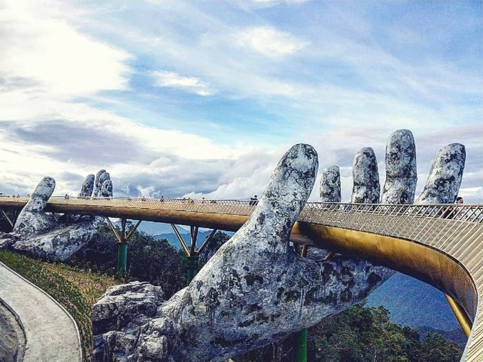 Cầu cầu trên mây ở Bà Nà Hills Đà Nẵng nằm giữa lưng chừng trời tại độ cao hơn 1.400m khiến bạn choáng ngợp bởi sự kỳ vĩ của không gian vô tận và khoảng không gian xanh mát xanh, bạn ngỡ mình đang đi lạc vào trốn bông lai tiên cảnh. Hai bàn tay khổng lồ nâng đỡ cây cầu uốn quanh giống như người thiếu nữ đang nâng dải lụa vắt ngang qua rừng núi