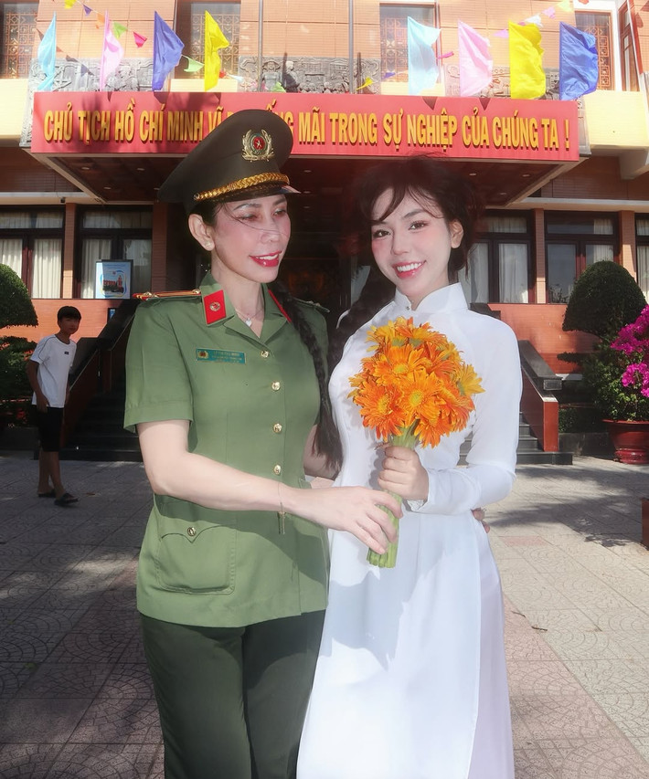 Cả hai cùng nở nụ cười tươi tắn, tay cầm bó hoa hướng dương, tạo nên một khung hình vừa ấm áp, vừa đầy tự hào.