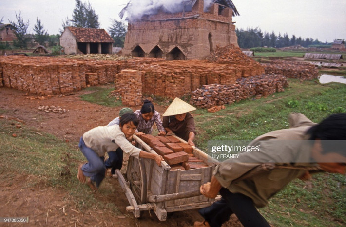 Cậu bé phụ người lớn đẩy xe chợ gạch tại một lò gạch.
