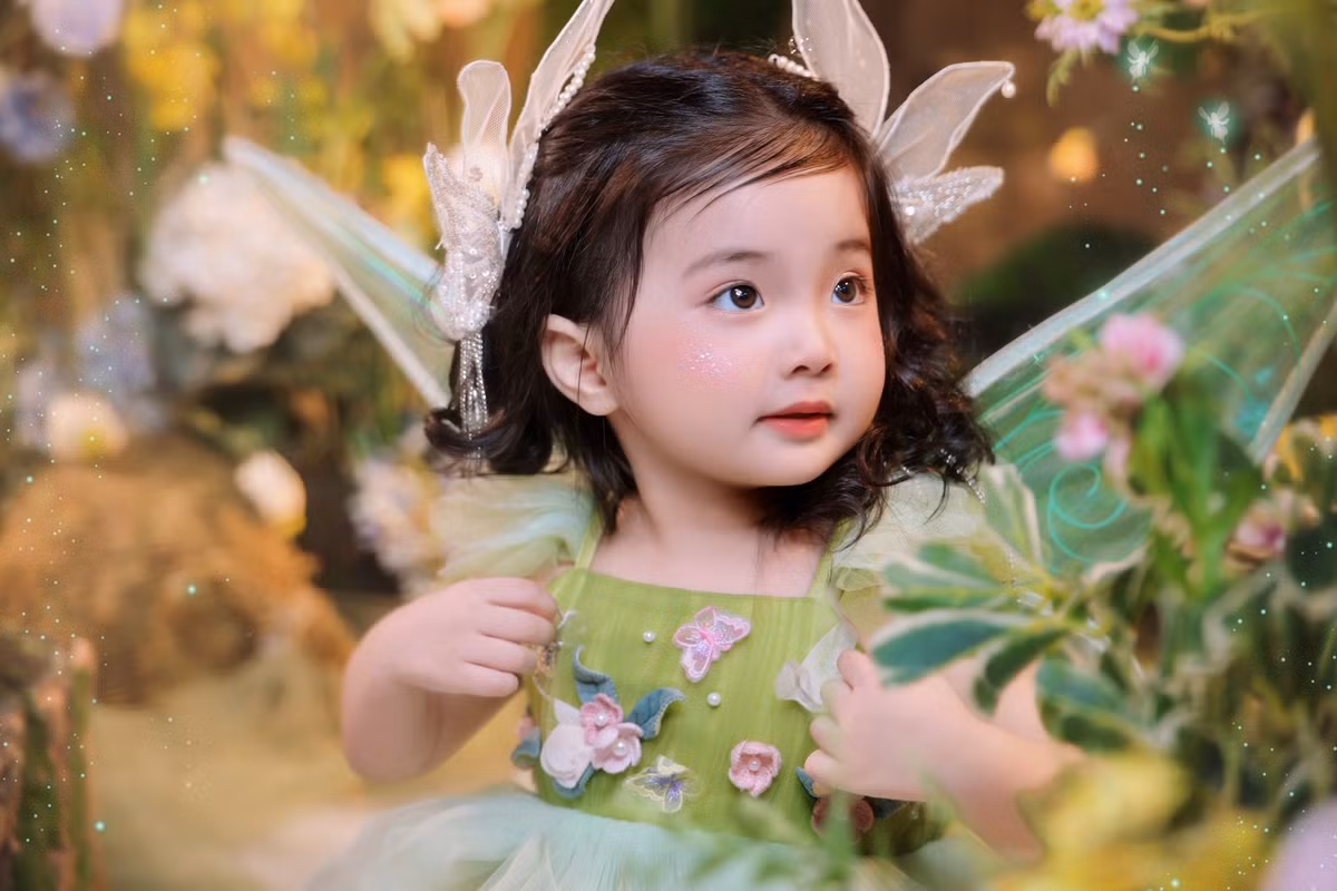 Trong loạt hình, bé Lisa diện váy xòe bồng bềnh, đeo cánh thiên thần tông xanh dịu mát, mái tóc xoăn lọn nhỏ càng làm nổi bật vẻ đáng yêu như một nàng công chúa bước ra từ truyện cổ tích.
