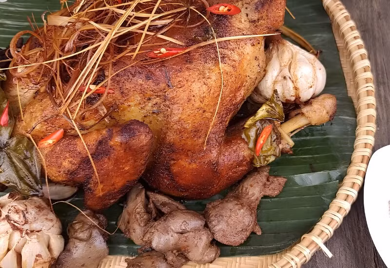 Không chỉ có các món nước, An Giang còn nổi tiếng với gà đốt lá chúc Ô Thum. Gà được tẩm ướp sả, ớt, tỏi rồi đốt trong nồi đất cùng lá chúc, giúp thịt giữ được độ mềm ngọt và lớp da vàng óng hấp dẫn. Hương thơm đặc trưng của lá chúc khiến món ăn trở nên khác biệt, nhất là khi dùng cùng xôi đậu xanh, rau rừng và muối tiêu chanh. Ảnh: Arttimes