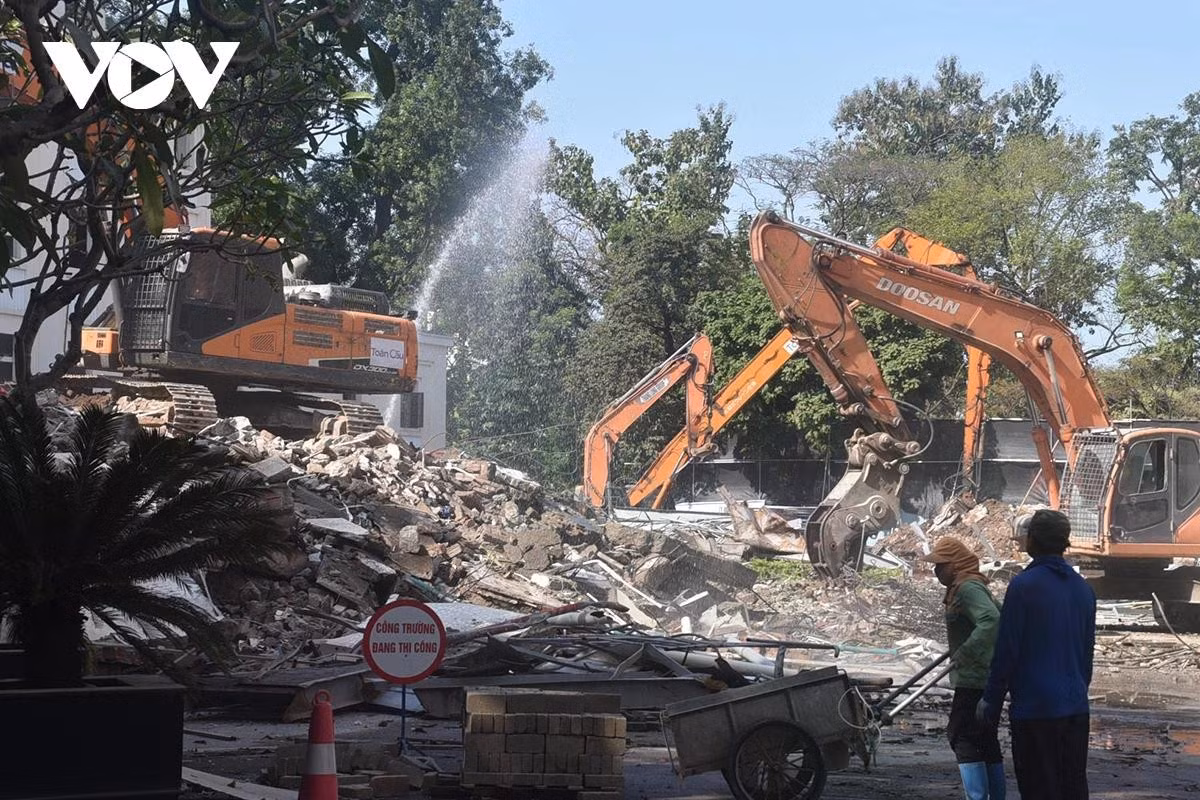 Máy xúc liên tục gạt, gom các khối bê tông và vật liệu xây dựng sau khi công trình bị phá bỏ.