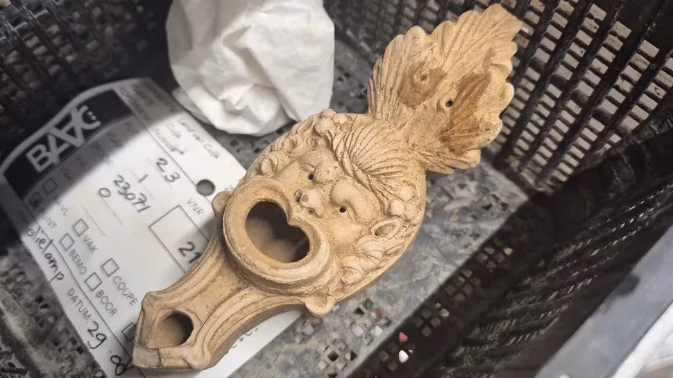 Theo các chuyên gia, chiếc đèn dầu có niên đại vào thế kỷ thứ 2 sau Công nguyên. Lỗ đổ dầu - nơi dầu được dầu đổ vào trông giống như một cái miệng lớn. Trong khi đó, tay cầm phía trên khuôn mặt giống như một chiếc lá lạ mắt. Ảnh: BAAC/RAAP.