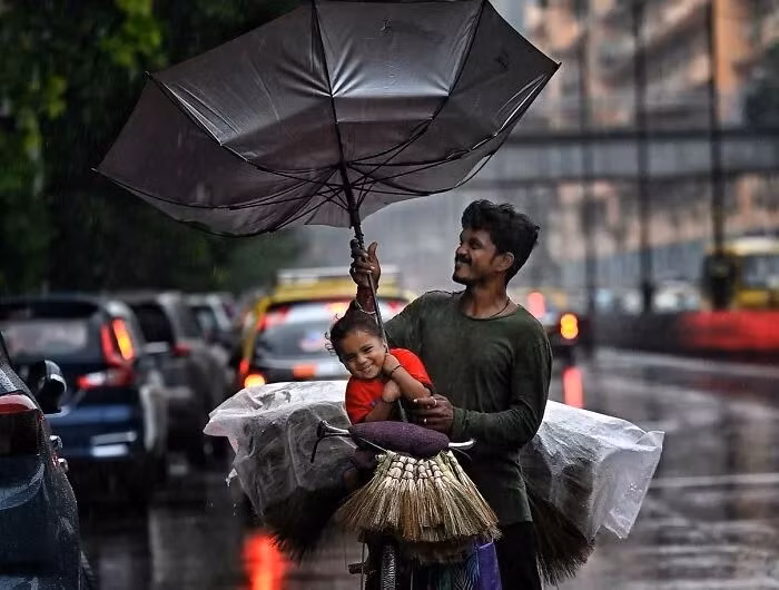 Người bán chổi và cô con gái nhỏ của anh đi dưới trời mưa gió gần ga Chhatrapati Shivaji Maharaj ở Mumbai.